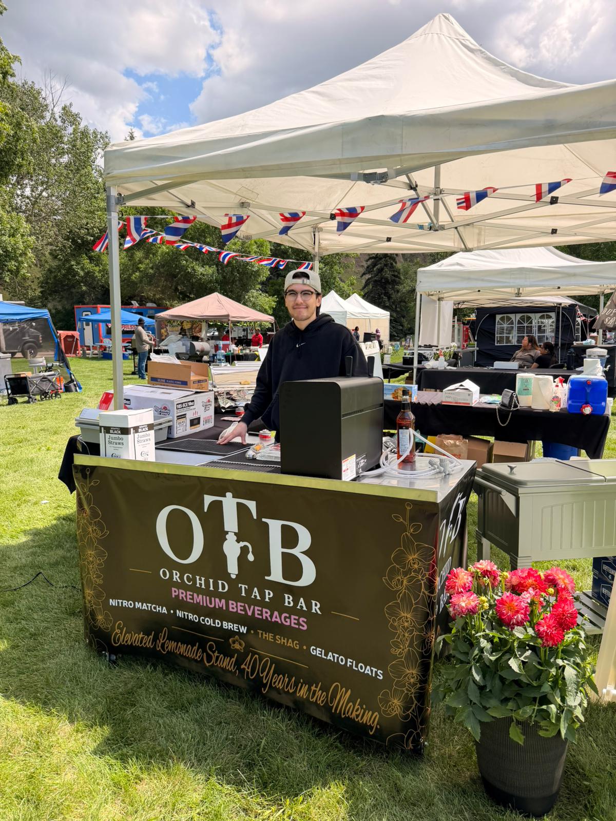 The Orchid Tap Bar booth with its branded banner, serving under a tent at a daytime festival