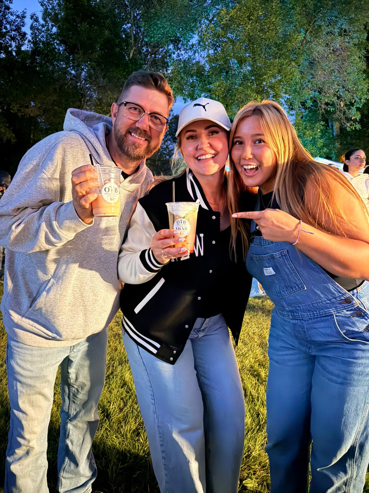 Three friends laughing together, holding OTB drinks at dusk