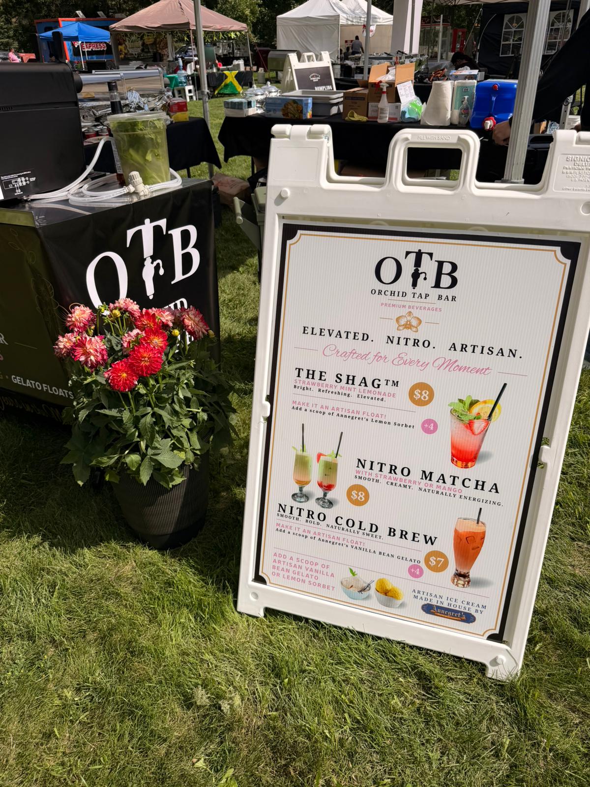 The OTB A-frame menu board beside fresh dahlias, listing The Shag, Nitro Matcha, and Nitro Cold Brew
