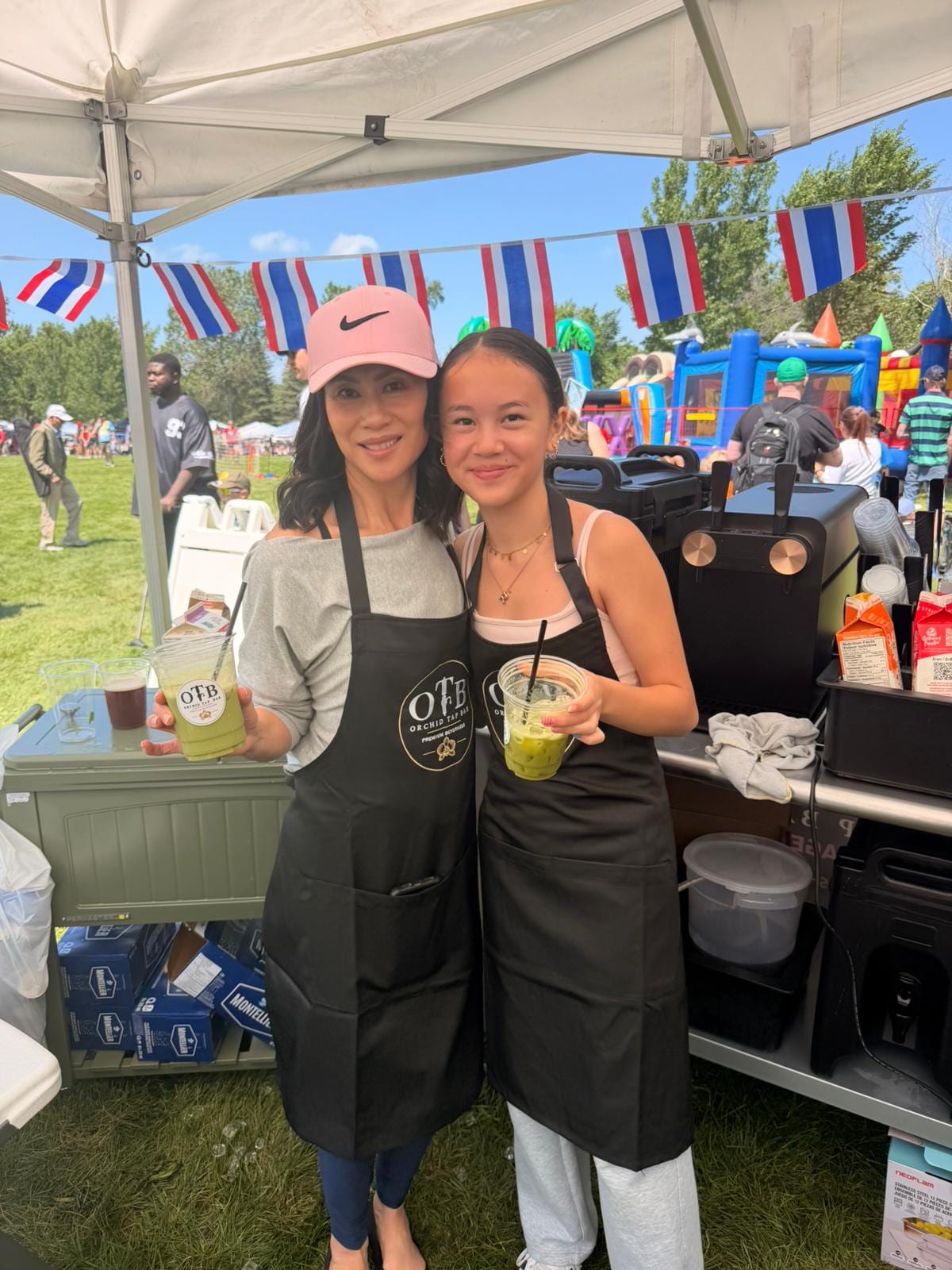 Two OTB team members in aprons behind the booth holding fresh matcha drinks