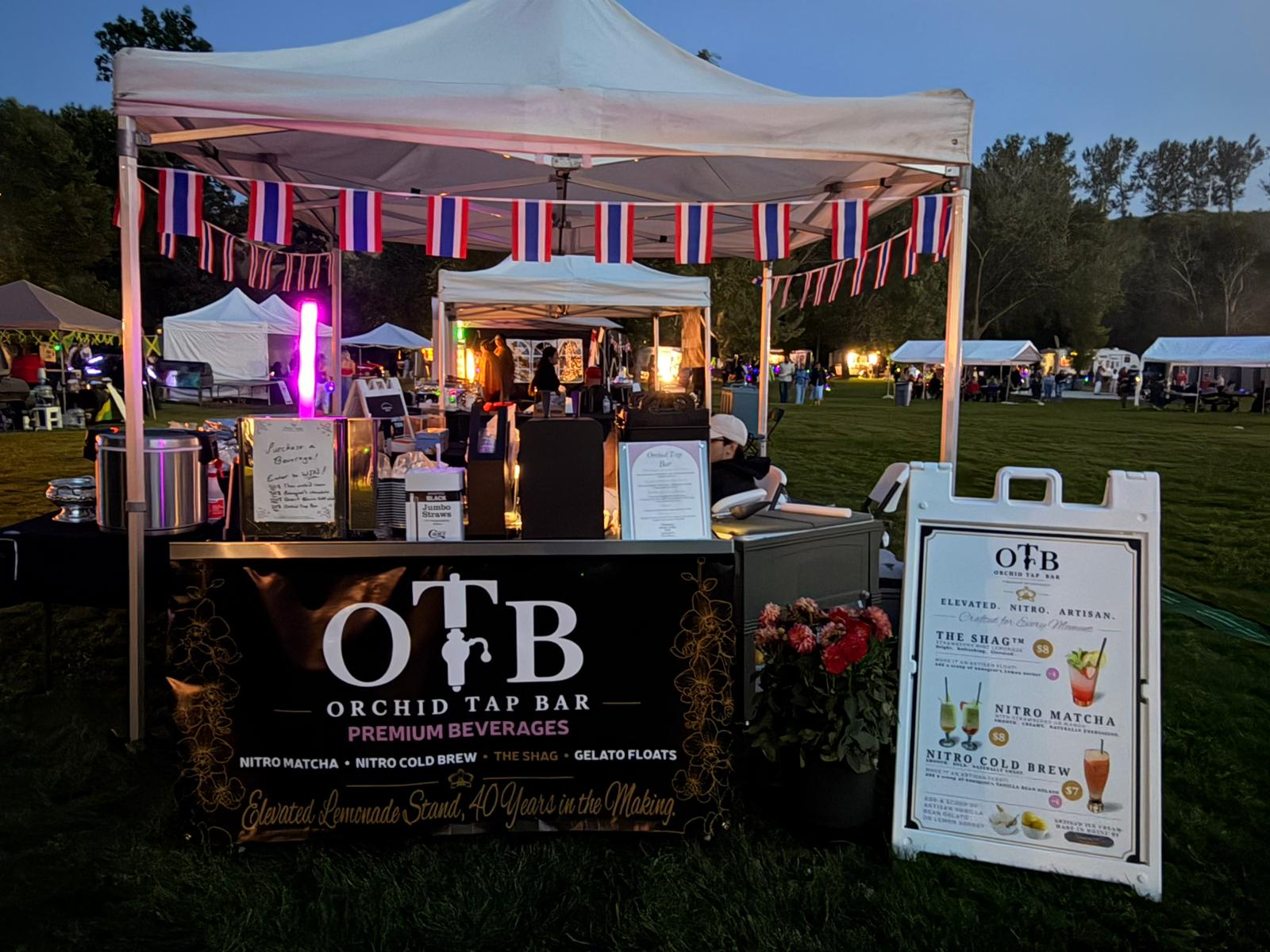 The Orchid Tap Bar booth glowing at dusk while serving guests at a community festival